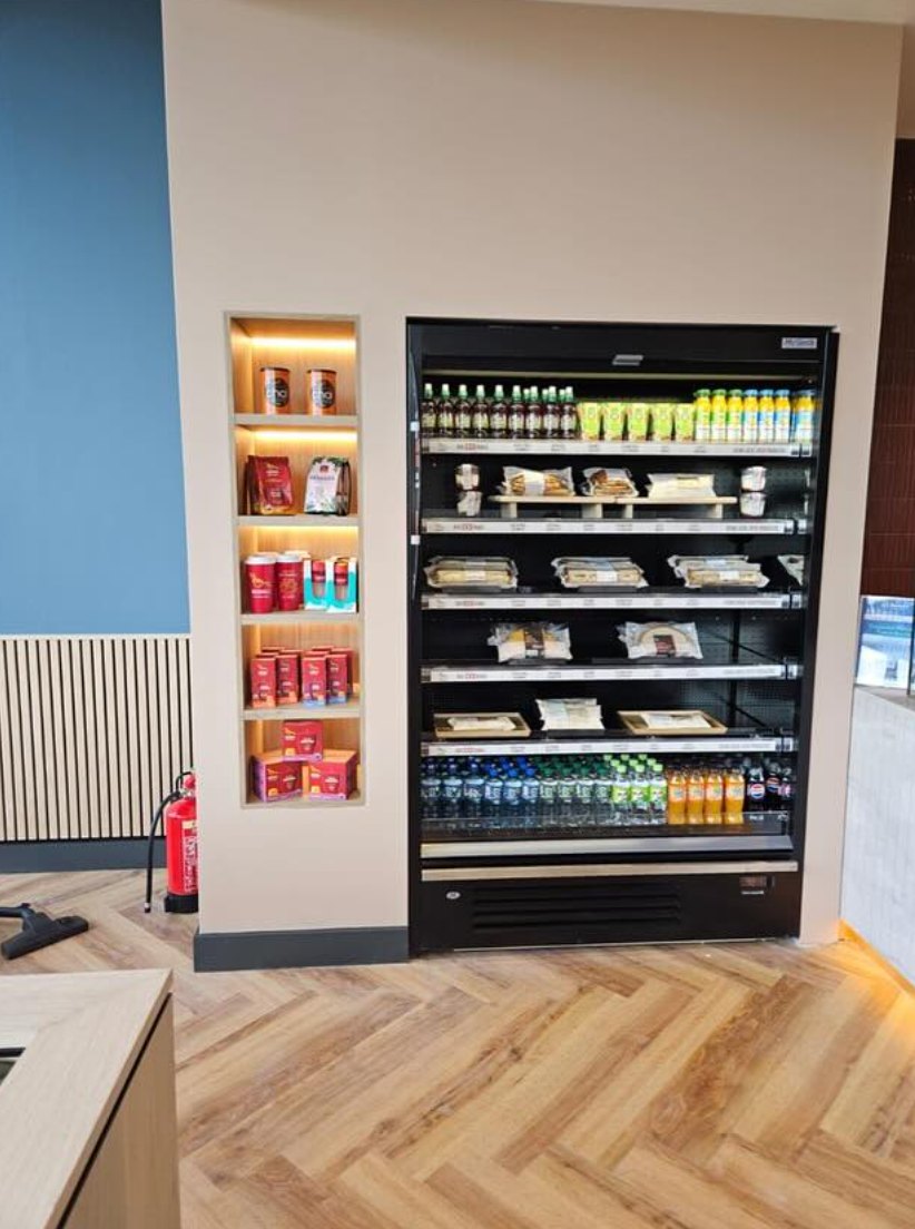 A lit chilled display and shelving by a wall